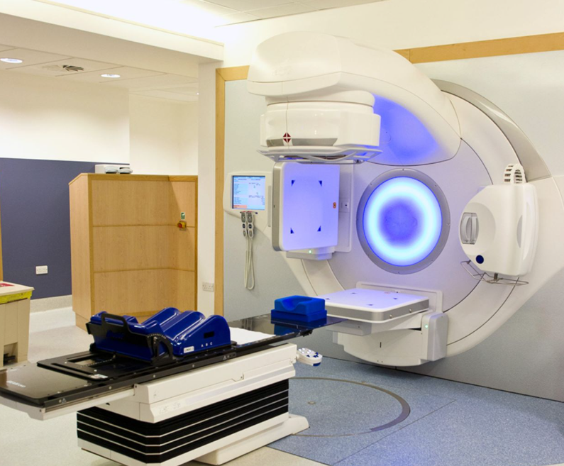 MRI scanner in a clinical room with a patient table extended, blue headrest visible on the table nearby