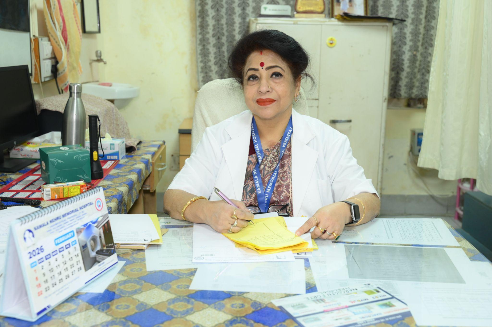 Healthcare professional sitting at a cluttered desk, signing papers with a pen.