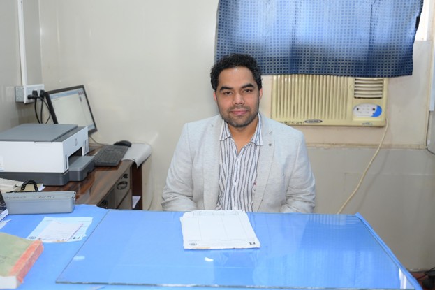 Healthcare professional sitting at a cluttered desk, signing papers with a pen.